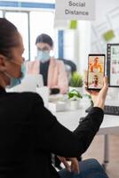 Businesswoman having online videocall meeting conference with remote friends using smartphone working in company business office. Teamwork wearing medical face mask to prevent infection with covid19 photo