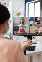 Executive manager with medical face mask discussing management statistics with remote team having online videocall meeting conference on laptop working in startup office. Teleconference on screen photo