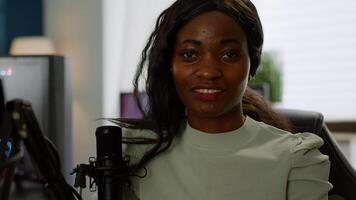 Black woman gamer looking at camera smiling and playing virtual shooter game championship in cyberspace, esports player performing on powerful computer in stylish room during gaming tournament photo