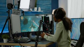 Black woman streamer playing space shooter videogames with joystick talking with teammates on streaming open chat. Cyber performing on RGB powerful computer in gaming room using professional equipment photo