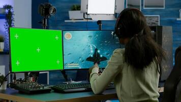 African gamer playing virtual videogame on powerful computer, chatting on green screen mock up, chroma key display. Cyber player using pc with isolated desktop streaming shooter games wearing headset photo