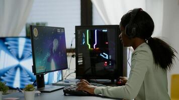 Excited black woman gamer sitting on desk, having headset with mic playing space shooter game. Online streaming cyber performing on powerful personal computer during gaming tournament photo