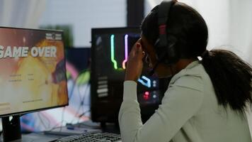 Furious african woman gamer with headset losing space shooter game with graphics during gaming championship playing from home at RGB powerful personal computer, performing at esports tournament photo