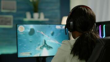 Closeup of competitive black woman player holding joystick playing space shooter game at powerful computer late night. Professional gamer using wireless controller for online gaming championship photo