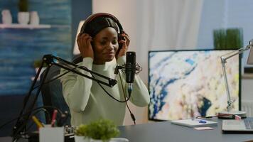 African blogger smiling at audience while filming podcast, looking at camera putting on headset. On-air production internet broadcast host streaming live content, recording digital social media photo