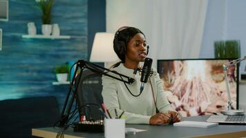 Black woman host of online show looking in laptop talking in podcast microphone with listeners entertainment. Speaking during livestreaming, blogger discussing in vlog wearing headphones. photo