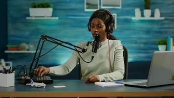 Black blogger woman recording for her blog in home studio reading messages checking sound on mixer. On-air online production internet broadcast show host streaming live content for social media photo