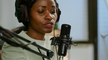 Close up of afro woman vlogger making new blog in home studio talking in professional microphone with audience. Speaking during livestreaming, blogger discussing in podcast wearing headphones. photo
