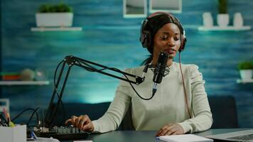 African influencer recording content using professional sound mixer and micophone in home studio. Speaking during livestreaming, blogger discussing in podcast wearing headphones. photo