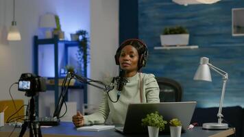 African social media woman looking in laptop talking at microphone recording podcast for youtube channel using camera. Online show On-air production internet broadcast host streaming live photo
