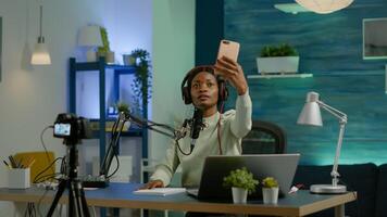 African content creator taking photo with smartphone for fans and recording broadcast. On-air online production internet podcast show host streaming live content, recording digital social media.