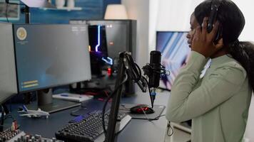 African woman streamer cyber putting on headphones performing space shooter game on RGB powerful computer talking with players on stream chat with microphone in gaming competition. photo