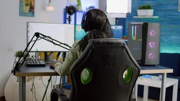 Back shot of streamer woman playing on powerful computer shooter game for tournament, talking with multiple players into headphones. Pro gamer using professional streaming equipment photo