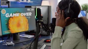 African videogame streamer losing online competition wearing professional headset talking on stream chat. Sad gamer using powerful computer for gaming tournament late night playing space shooter game photo
