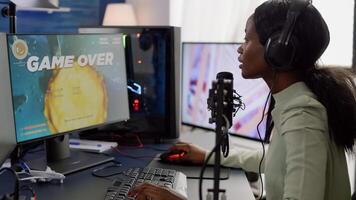 African streamer woman playing on powerful RGB computer shooter game losing tournament, talking with multiple players into headphones. Pro gamer using professional streaming equipment photo