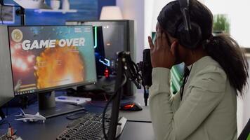 Furious black woman gamer with headphones using stream chat losing game playing on RGB powerful computer shooter game. Virtual online streaming cyber checking sound performing in gaming tournament photo