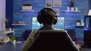 Back shot of streamer woman playing on RGB powerful computer shooter game for tournament, talking with multiple players into headphones. Pro gamer using professional streaming equipment photo