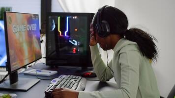 Upset videogame african player losing online videogame competition wearing professional headset. Sad gamer using powerful RGB computer for gaming tournament late night playing space shooter game photo