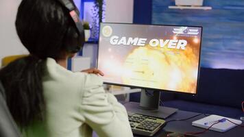Nevous pro african cyber losing videogame, game over for woman playing online space shooter games with headset. Player performing on RGB computer talking with players on chat in gaming competition photo