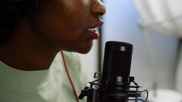 Close up of afro woman vlogger making new blog in home studio talking in professional microphone with audience. Speaking during livestreaming, blogger discussing in podcast wearing headphones. photo