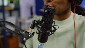 Close up of black woman influencer answering questions of audience while discussing with listeners using microphone. Speaking during livestreaming, blogger speaking in podcast wearing headphones. photo