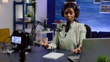 Portrait of african blogger woman talking with audience looking at professional camera working in podcast home studio. Content creator recording podcast, speaking during livestreaming photo