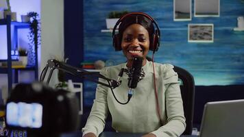 Close up of camera recording african influencer talking looking into it during online podcast. Social media content creator streaming online broadcast, blogger discussing wearing headphones. photo