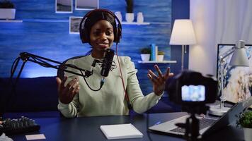Black blogger influencer recording blog concept waving and speaking looking at camera on tripod in home podcast studio. Social media vlogger shooting vlog, streaming online broadcast photo