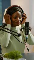 African blogger smiling at audience while filming podcast, looking at camera putting on headset. On-air production internet broadcast host streaming live content, recording digital social media photo