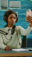 African woman using smartphone taking selfie in entertainment business recording episode. On-air online production internet podcast show host streaming live content, recording digital social media. photo