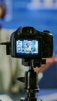 Close up of professional camera sitting in front of dslr recording online show. African woman vlogger speaking at microphone during livestreaming, blogger discussing in podcast wearing headphones photo