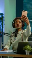 African content creator taking photo with smartphone for fans and recording broadcast. On-air online production internet podcast show host streaming live content, recording digital social media.