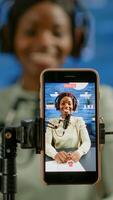 Close up of smartphone recording vlog of african influencer in home studio using smartphone. Speaking during livestreaming, blogger discussing in podcast wearing headphones and professional microphone photo