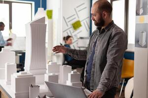 Architect contractor working in professional office with laptop computer for designing building model urban plan maquette. Professional businessman inspecting design project layout photo