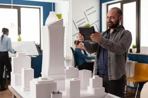 Work manager man looking on tablet at architecture office to design maquette construction layout building model. Professional constructor working on industry development project photo
