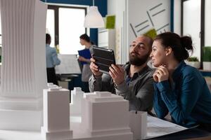 Design architecture colleagues sitting at office working on tablet and blueprints for layout plan maquette building model. Professional engineering team sitting for construction project photo