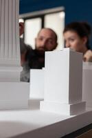 Talking architect team sitting at desk in professional office to work on building model maquette. Colleagues discussing plan of modern design architecture for layout project photo
