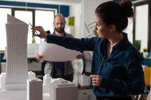 Architecture office partners looking at blueprints and plans for building model maquette. Caucasian professional workers pointing at construction design layout for urban project photo