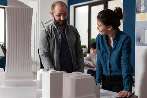 Architect work team talking at professional office standing at desk with maquette building model. Caucasian project partners looking to design blueprint for construction layout photo