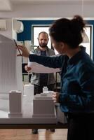 Architecture workers checking blueprints with maquette building model design plan. Caucasian workmates pointing at construction project layout for urban development business photo