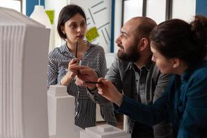 Group of engineer colleagues work in architecture at project with blueprint plans building model maquette. Professional partners discussing vision of construction design on paper photo