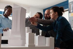 Group of multi ethnic colleagues work in architecture at project with blueprint plans building model maquette. Professional partners discussing vision of construction design on paper photo