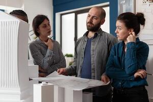 Architectural diverse work group talking about project design construction. Multi ethnic professional team working on maquette building model for engineering industry and business photo