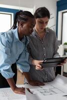 Team of architectural design women looking at tablet working on blueprint plan. Professional multi ethnic group analyzing construction layout project design for development work photo