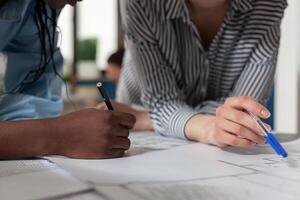 Close up of diverse architect women hands working on blueprint plans at desk. Professional engineer team designing construction layout for building model maquette project design photo