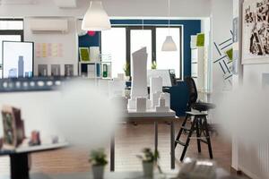 Empty architectural office with foam building model on table and computer screen with blueprints. Nobody in blue and white open space used by architect to design concept real estate. photo