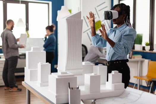 Architect using vr headest to look at white foam scale model of real estate project. Engineer working with augmented reality looking at table with skyscraper building maquette. photo