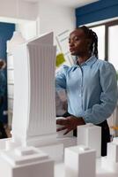 Portrait of architect looking at the architecture design of futuristic building at desk with residential project maquette. Engineer inspecting skyscraper model in architectural modern office. photo