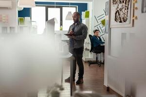Wide view of architectural engineer holding tablet looking in the distance thinking about improving construction plans. Architect inspecting the design of skyscraper building model in modern office. photo