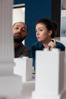 Professional architects team inspecting skyscraper white foam model design in architectural modern office. Project engineers colleagues lookin inspired in front of 3d residential maquette. photo
